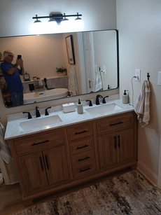 Bathroom with double vanity, light wood cabinets, black hardware, large mirror, and neutral color palette.
