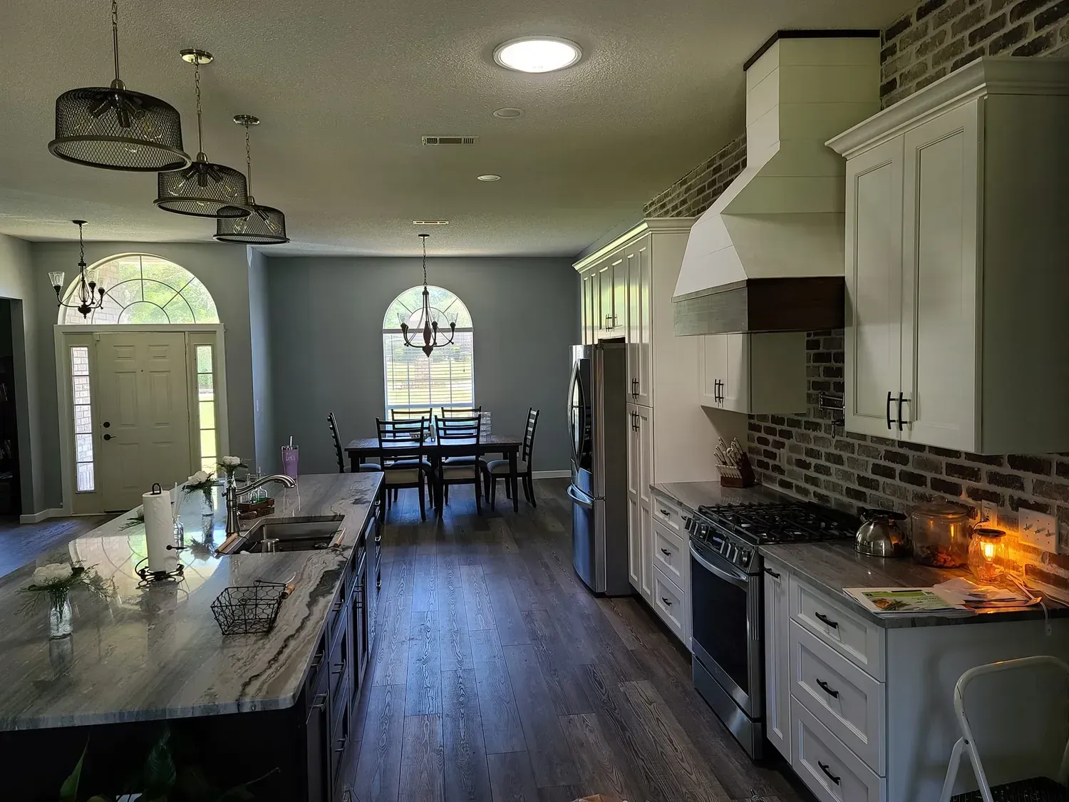 Long kitchen with white cabinets, stainless steel appliances, island, and dining area.
