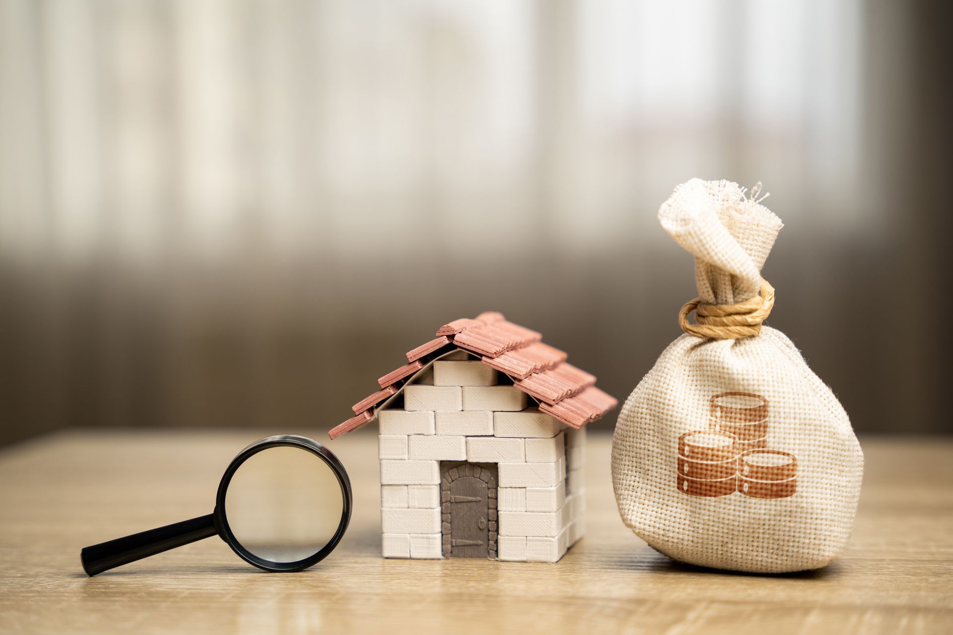 A magnifying glass , a model house , and a bag of money are on a table.