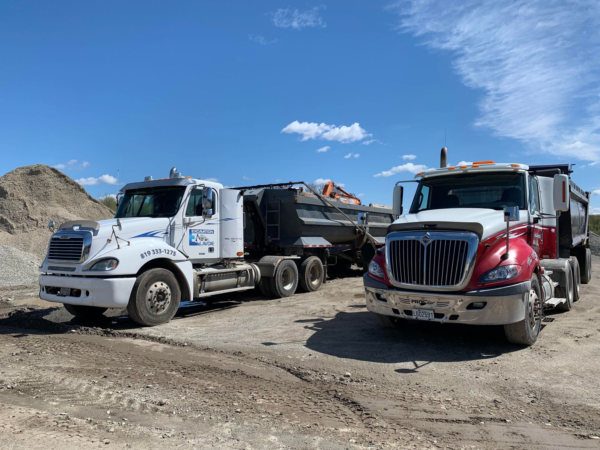 Deux camions à benne basculante sont garés l'un à côté de l'autre sur un chemin de terre.
