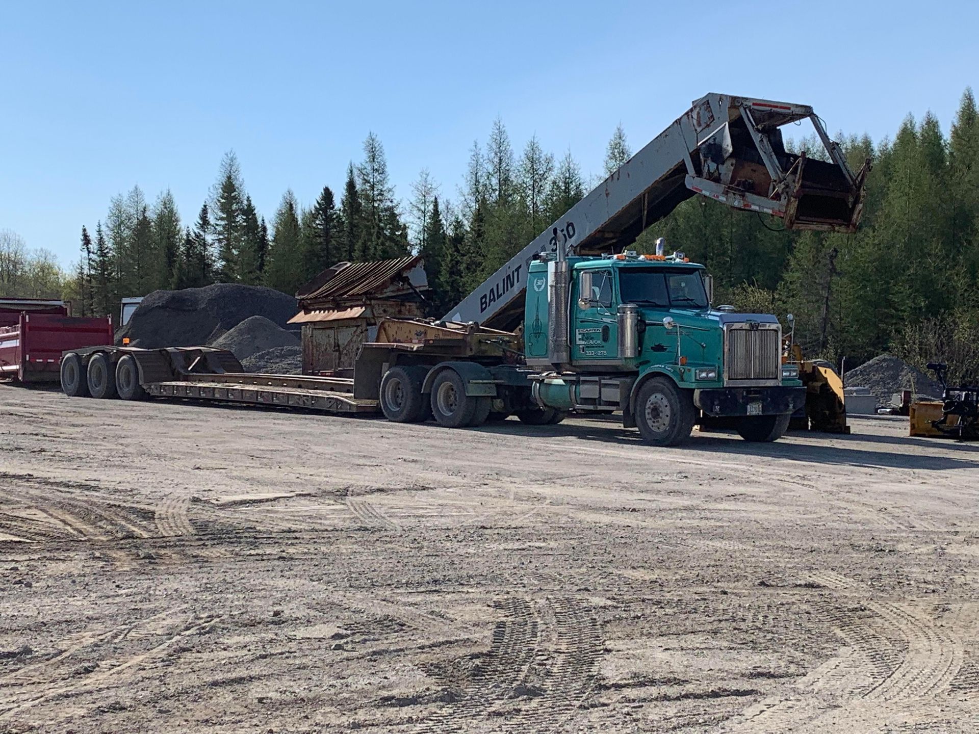 Un semi-remorque vert avec une grue attachée est garé sur un terrain en terre.