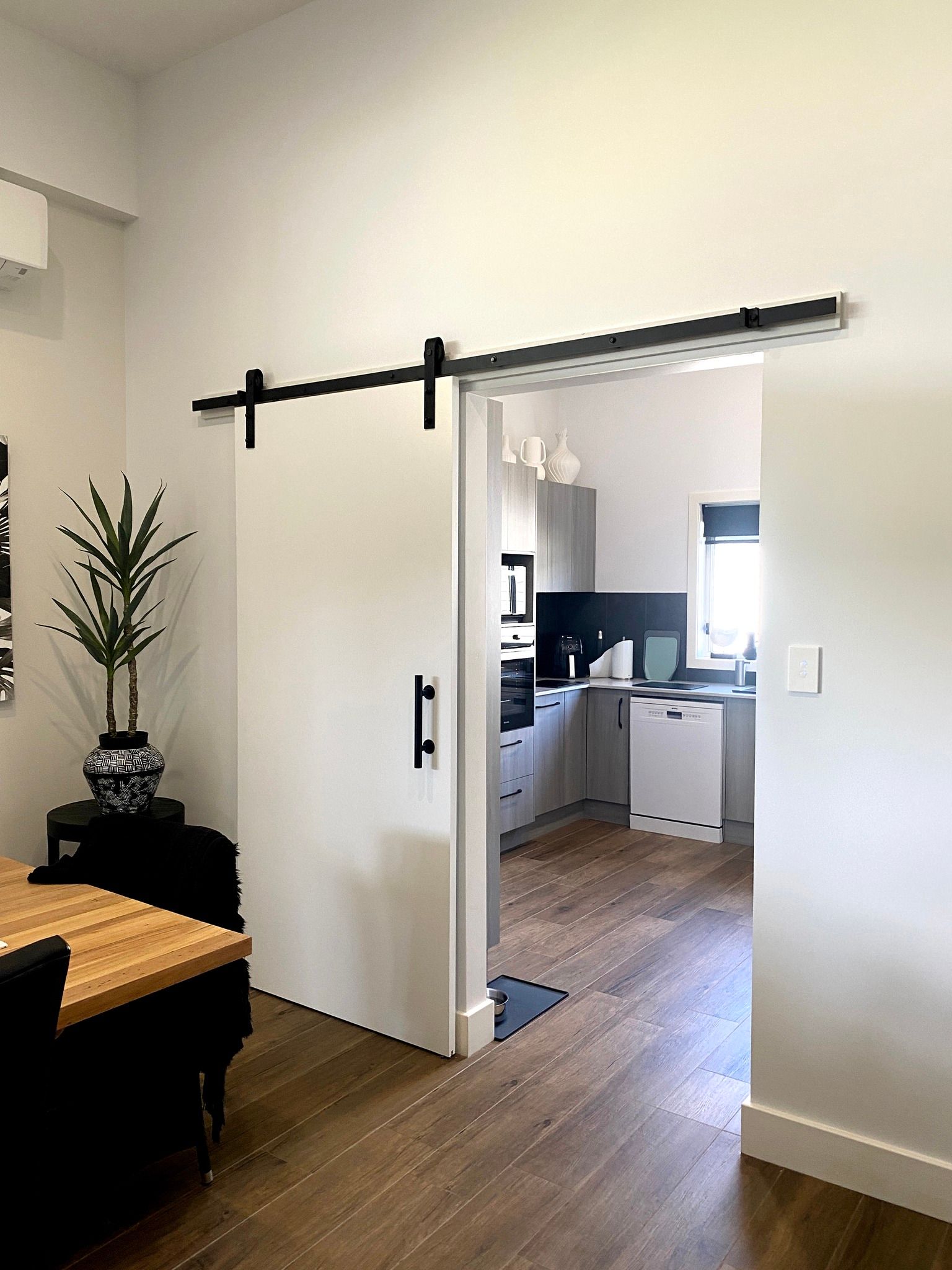 White Barn Door on a Black Track Partially Open to a Kitchen — BK Building Services Pty Ltd In Forster, NSW