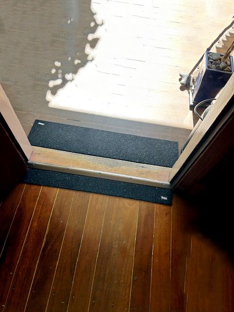 Wooden floor with a doorway threshold and two dark grey anti-slip mats, leading to a bright outdoor area — BK Building Services Pty Ltd In Forster, NSW