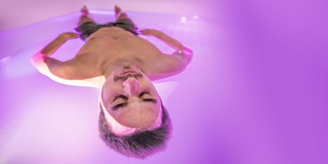 Mann schwebt mit geschlossenen Augen in einem Reizentzugstank, umgeben von violettem Licht.
