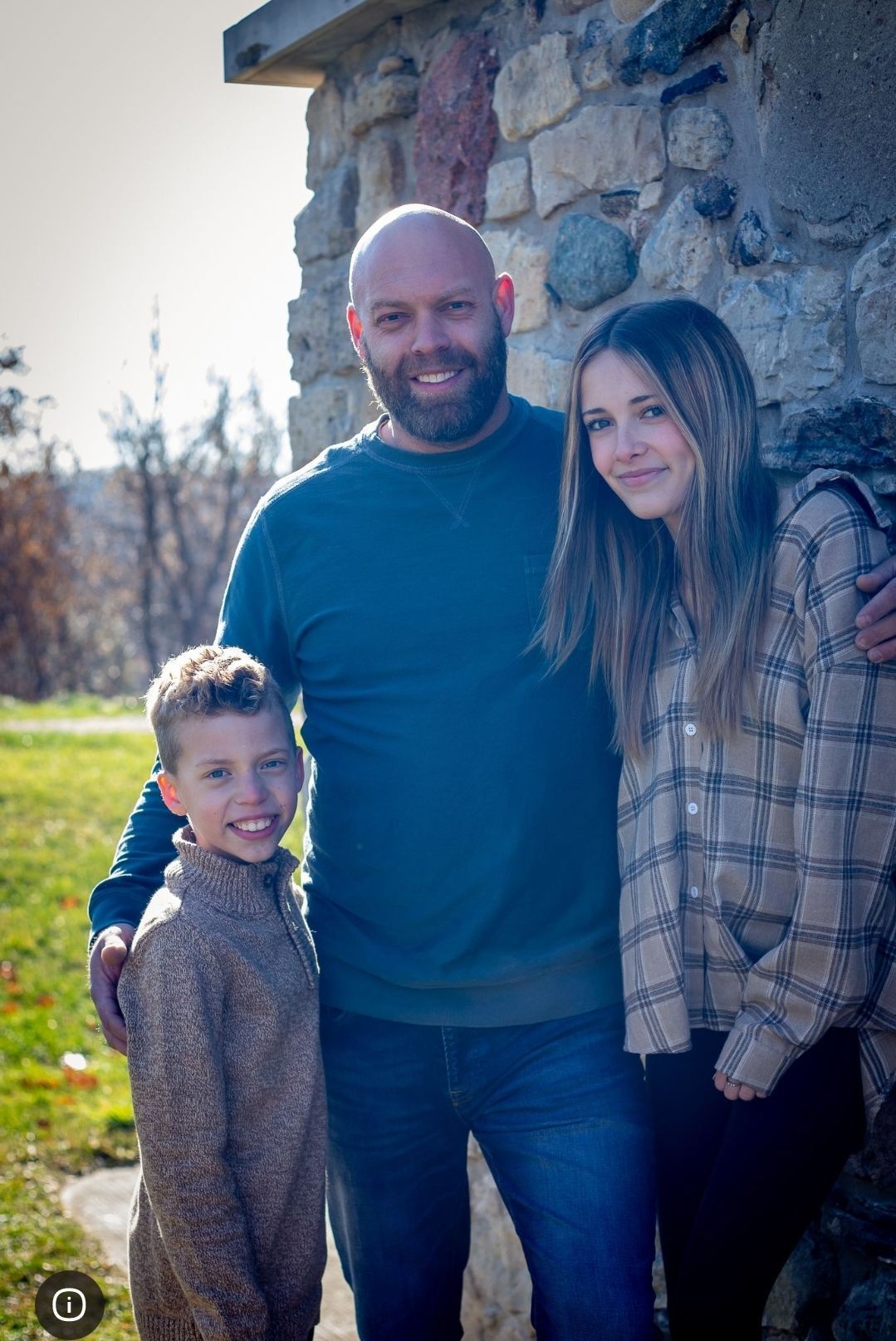 A man and two children are posing for a picture in front of a stone wall.