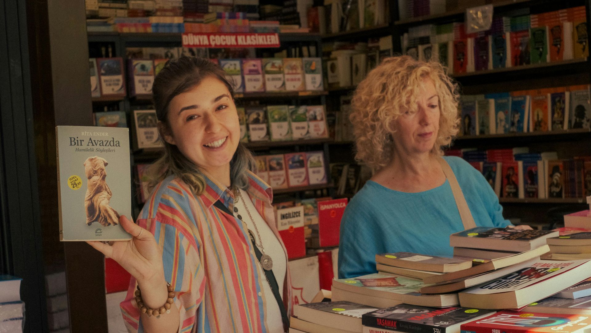 Two women are standing next to each other in a bookstore holding a book.