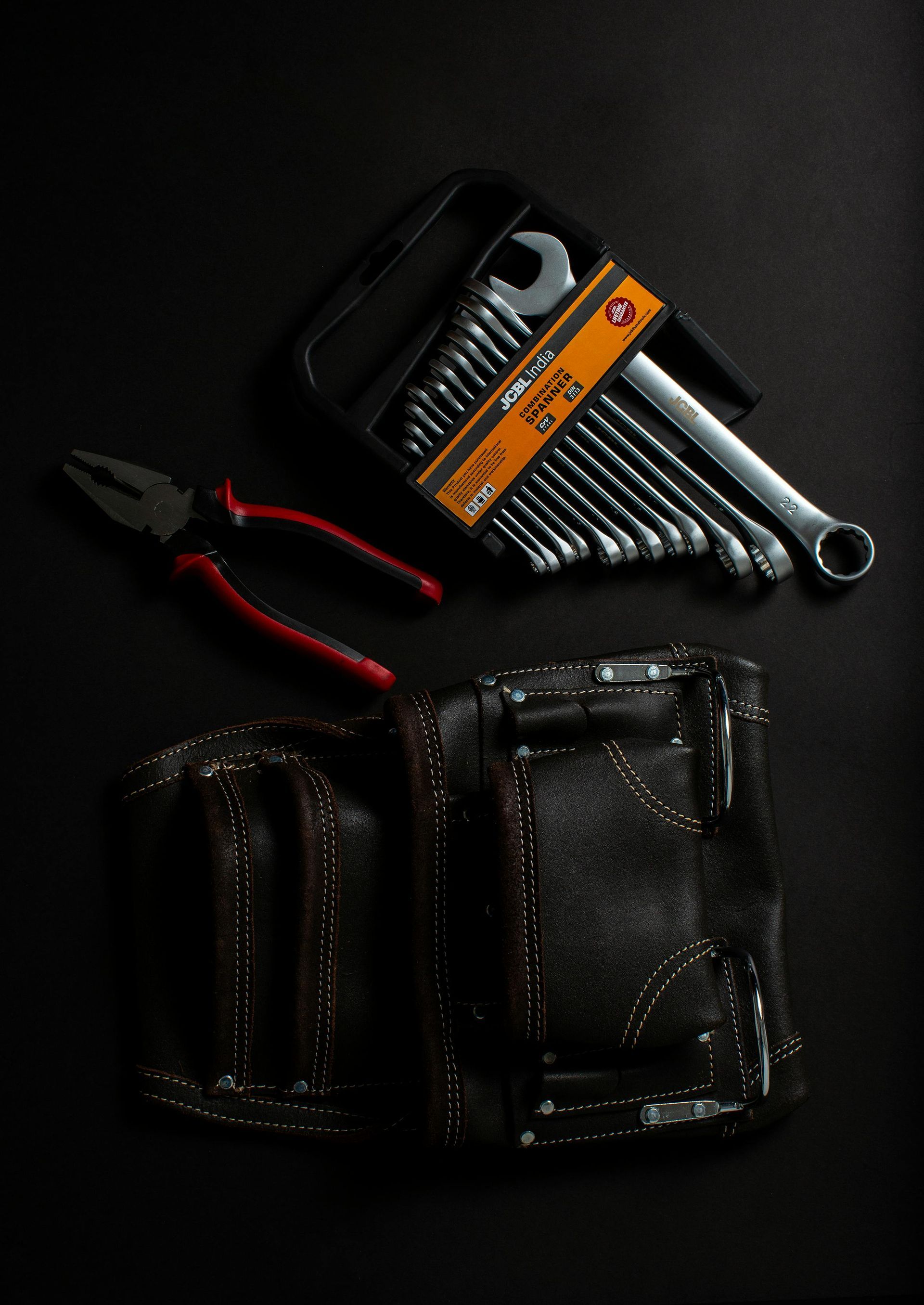 A pair of pliers , a set of wrenches , and a tool belt on a black background.