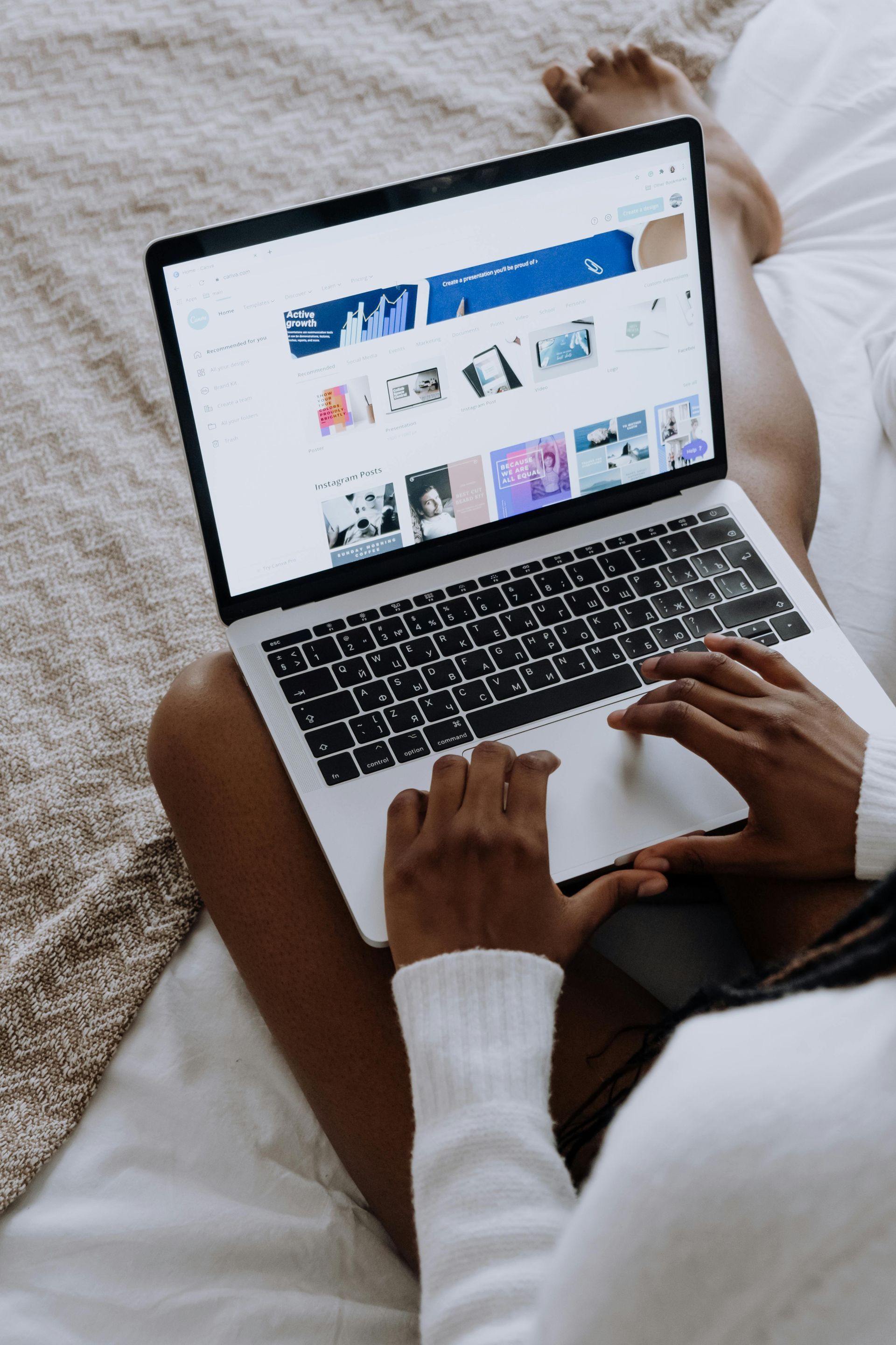 A woman is sitting on a bed using a laptop computer.