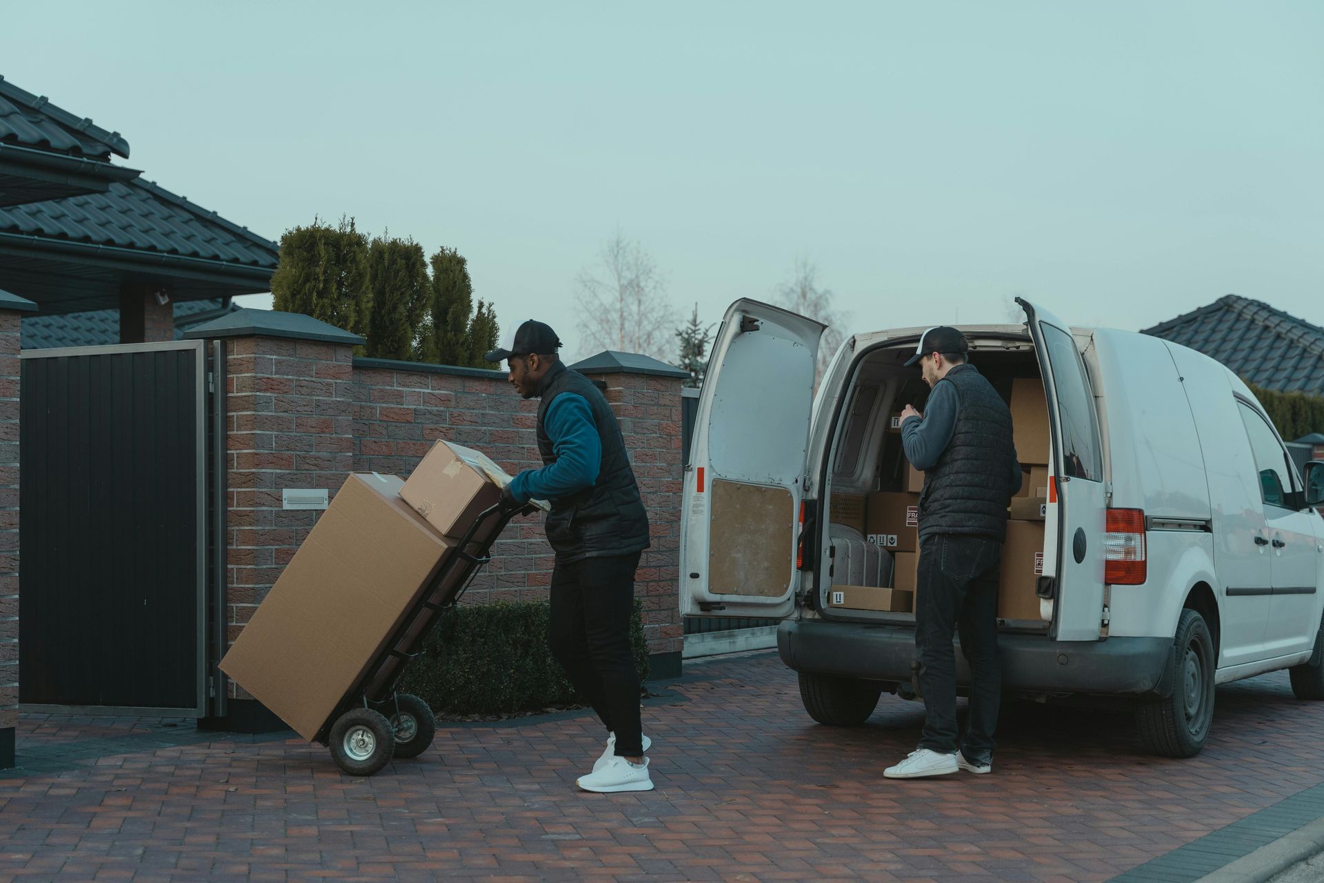 Two delivery men are loading boxes into a white van.