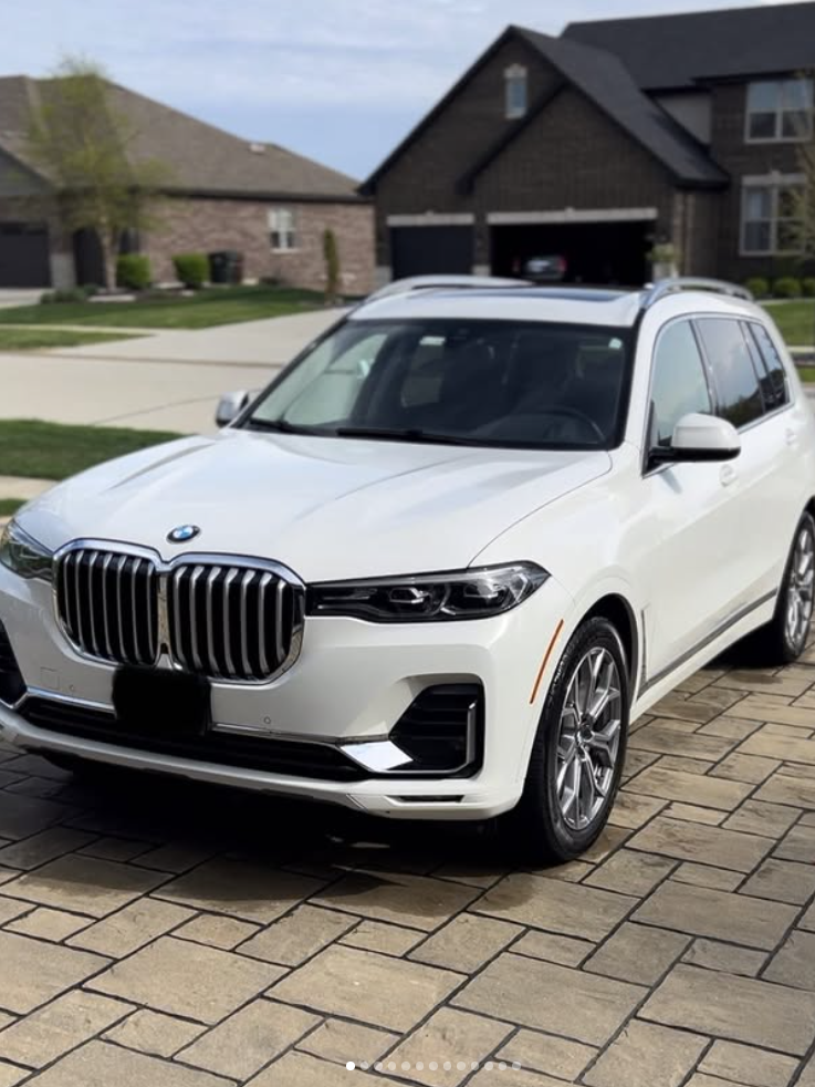A white BMW SUV parked on a paved driveway in front of a suburban house.