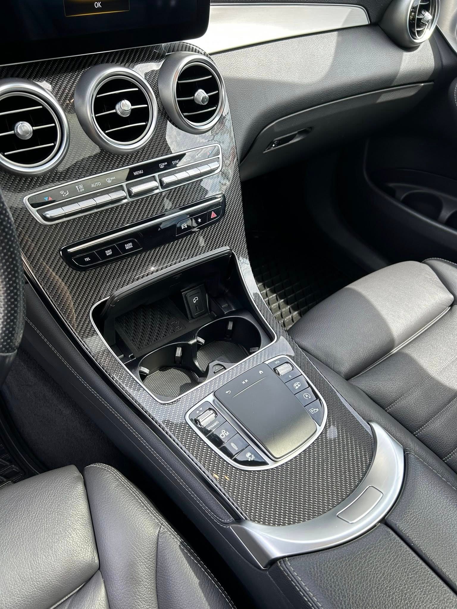 Interior of a Mercedes-Benz featuring a carbon fiber center console, circular air vents, and a digital infotainment pad.