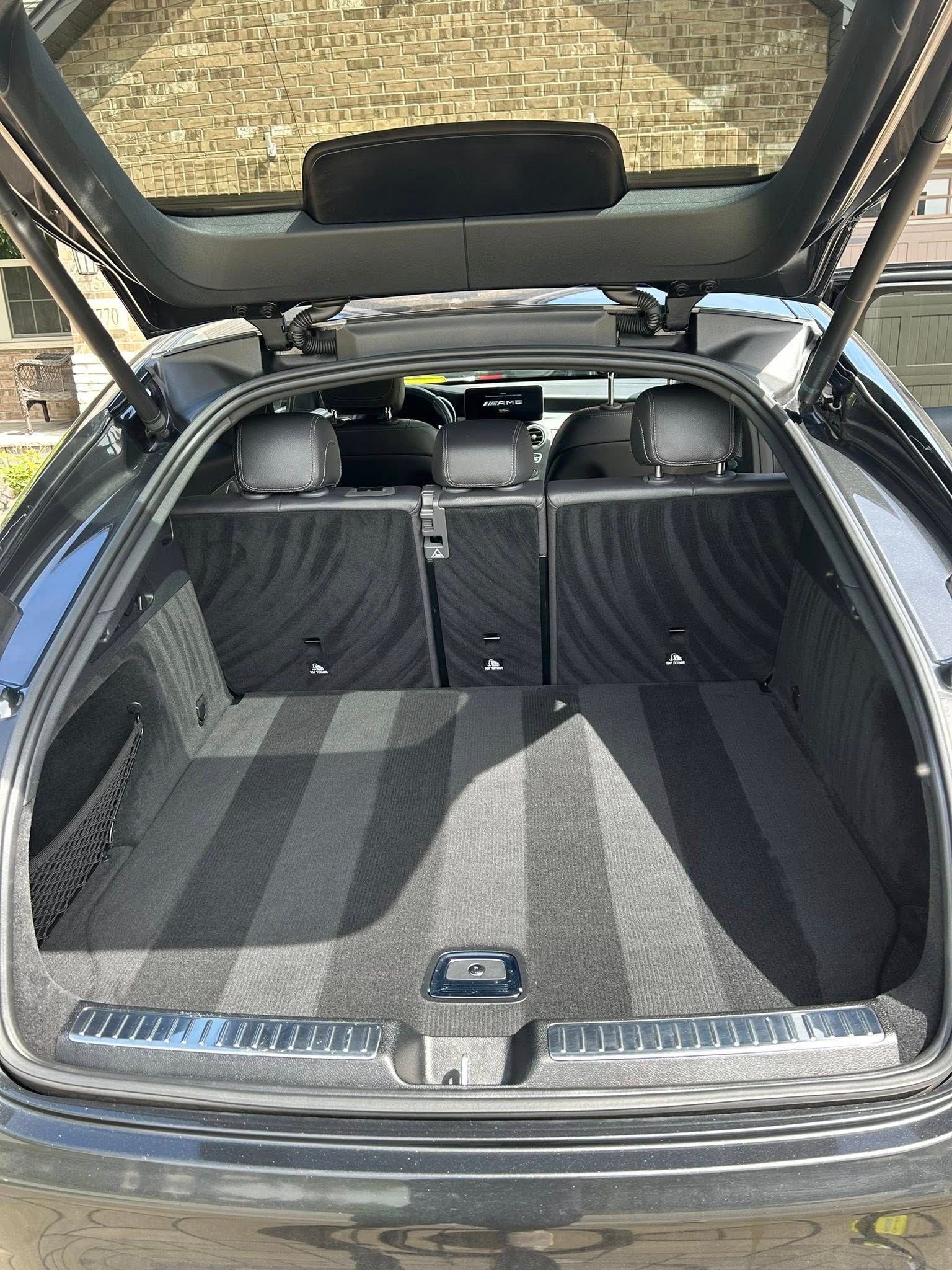 The open, carpeted trunk of a dark-colored luxury vehicle, showing folded rear seats and a tidy cargo area.