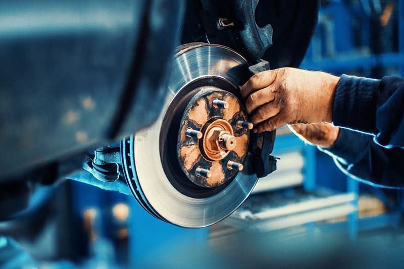 Mechanic working on a car's brakes in a garage; hands holding brake pad, rotor visible.
