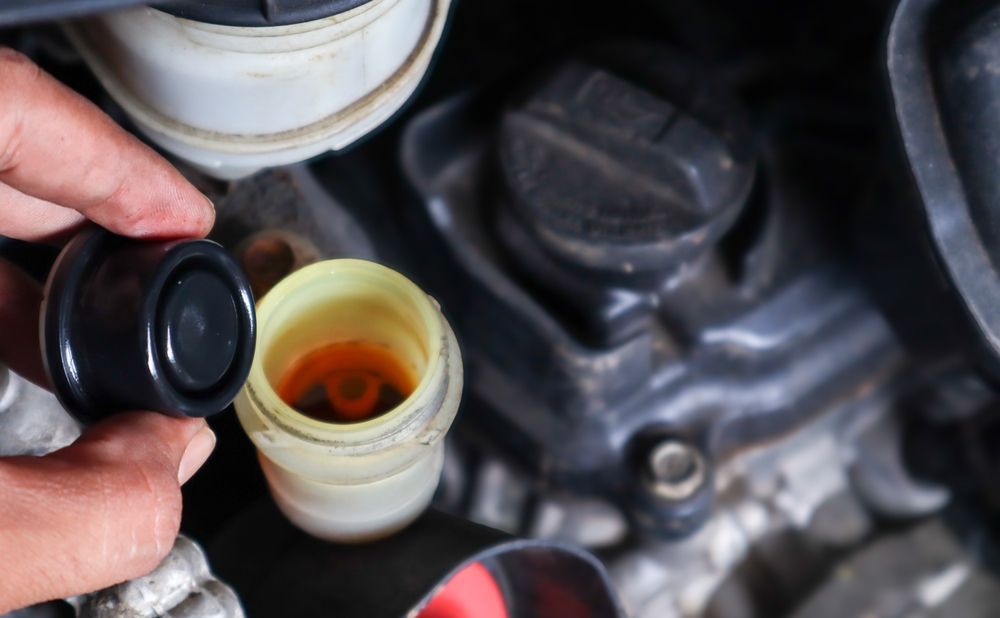 Hand opening car brake fluid reservoir, revealing amber fluid.
