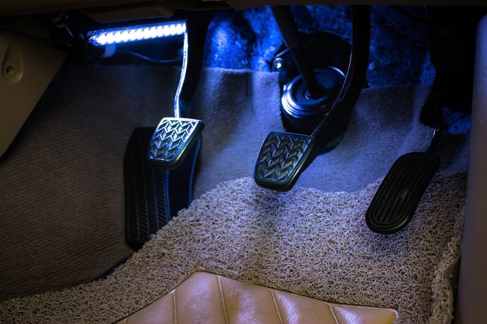 Car interior with blue LED lighting illuminating the gas, brake, and clutch pedals.