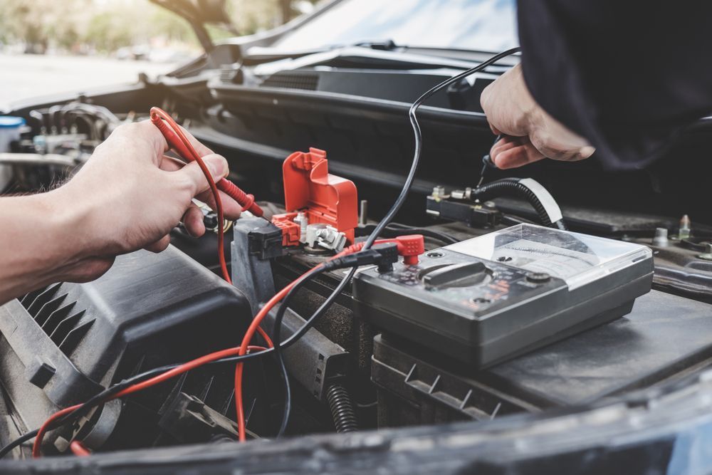 Hands Using a Multimeter to Test a Car Battery in an Engine Bay — Ottos Mufflers in Noosaville, QLD