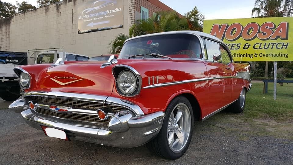Red and white 1957 Chevrolet Bel Air parked in front of a shop with a 