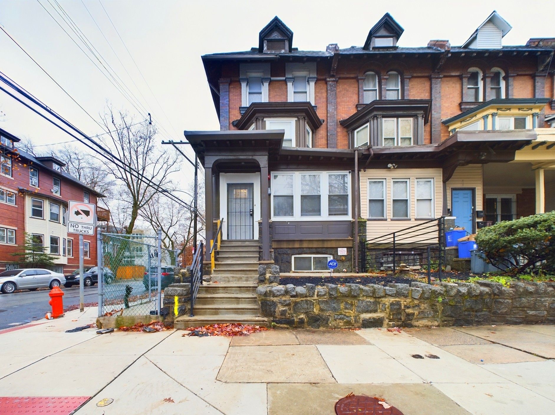 Victorian-style end-unit rowhome with porch, stone base, and corner city sidewalk.
