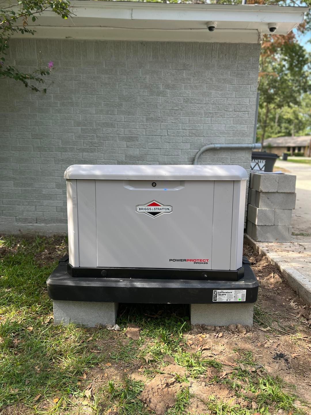 Gray generator on a black base, brick building background, outdoor setting.