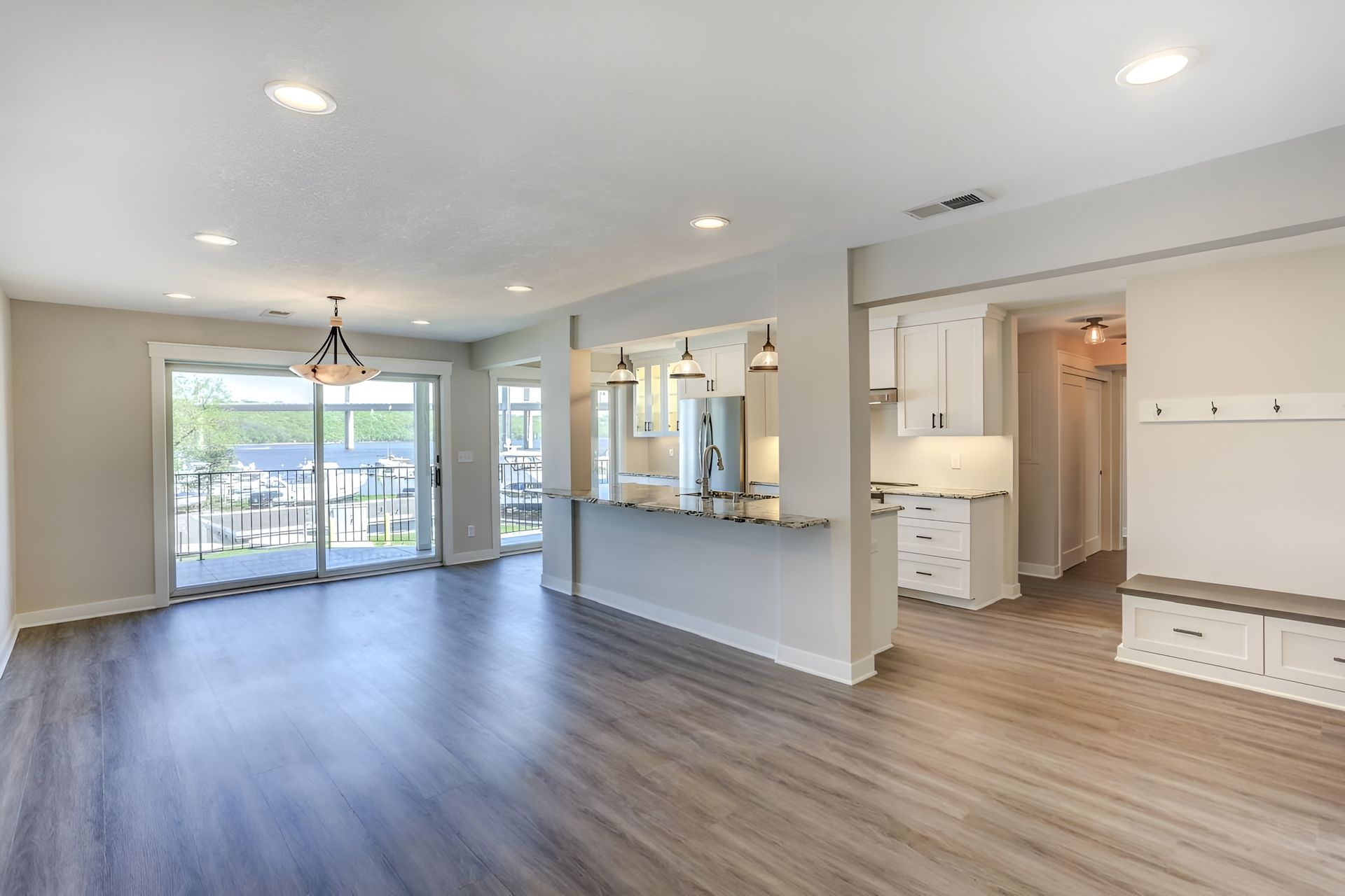 Open-concept living space with gray wood-look floor, kitchen bar, and sliding glass door to a balcony.