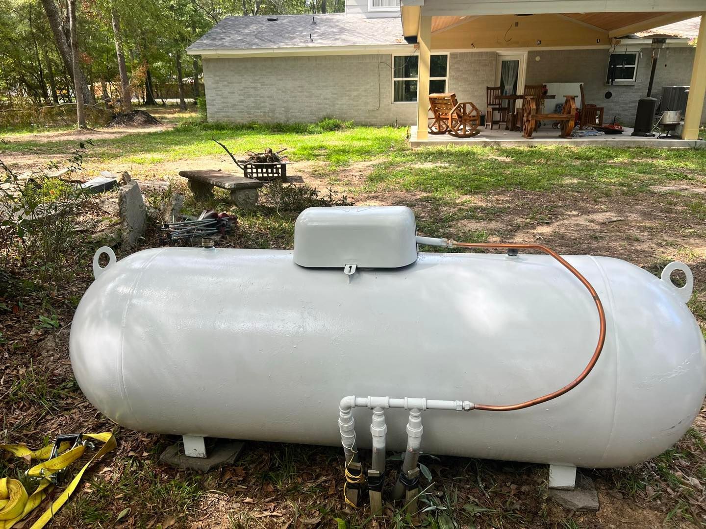 Large white propane tank in a yard, connected to a house with a covered patio.