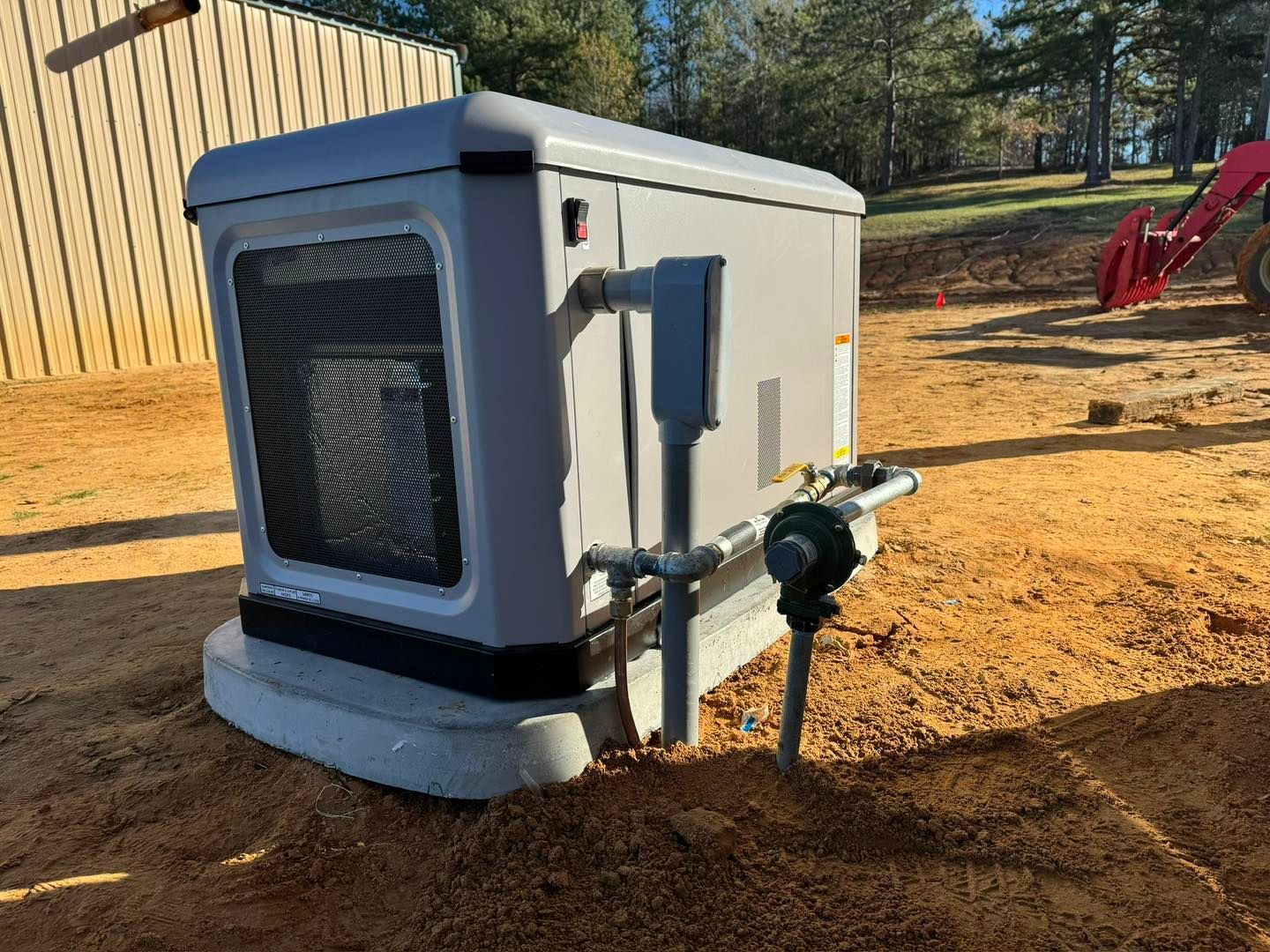 Gray generator on a concrete base, installed outdoors on dirt and sand.