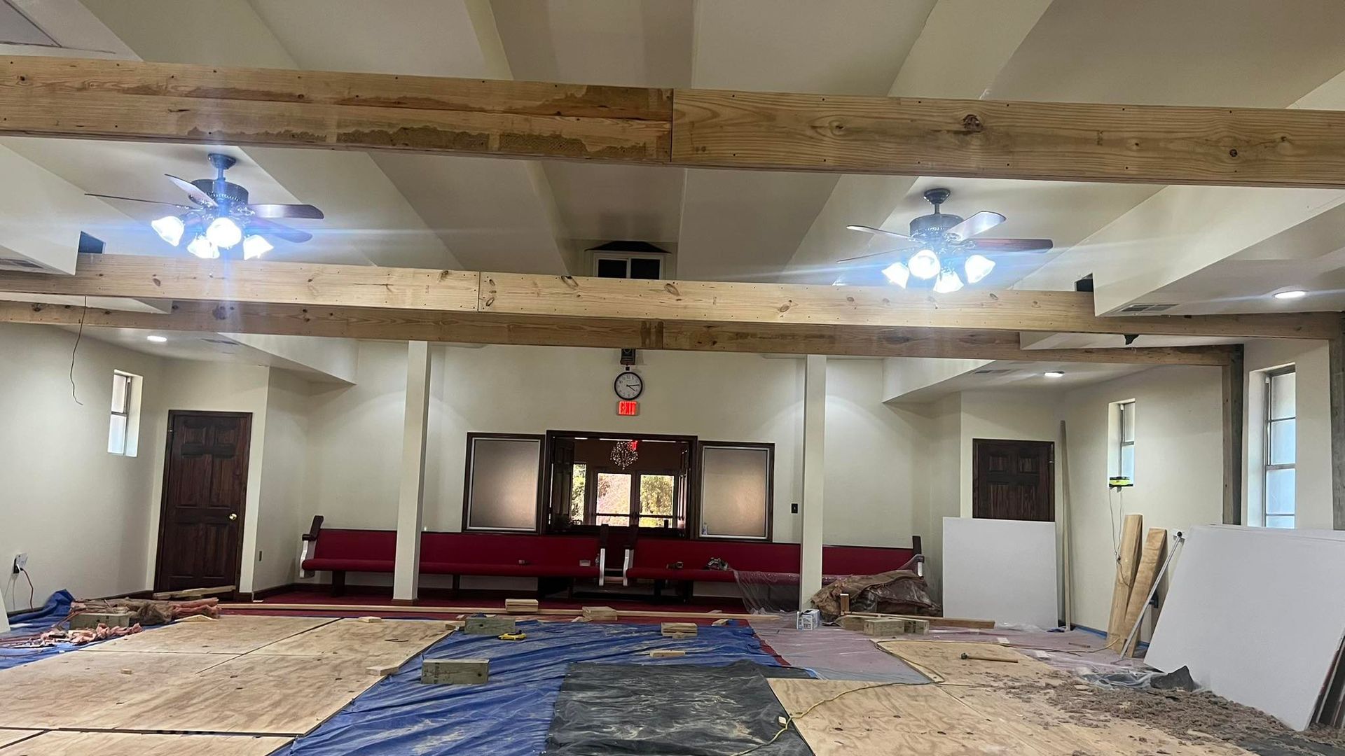 Interior of a room under construction with exposed beams, ceiling fans, and an altar at the far end.