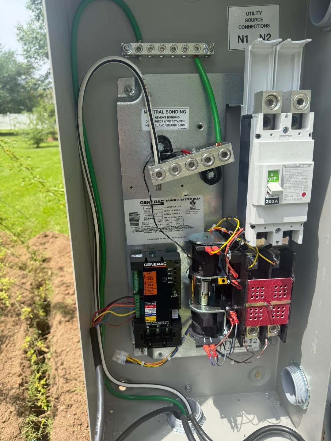 Open electrical panel with wires and circuit breakers. Green grounding wire visible. Outdoor setting.