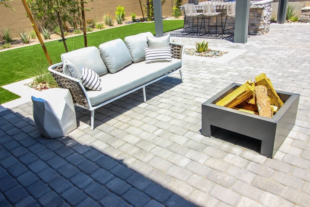 Outdoor patio with a gray sofa, fire pit, and stone pavers.