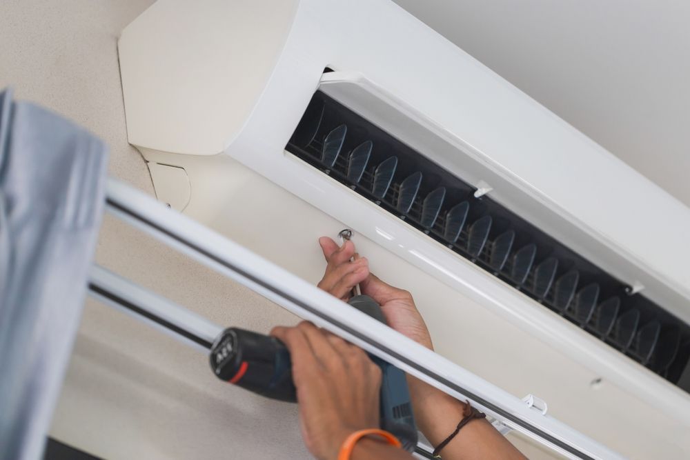 Person using a power drill to install or repair an air conditioner unit on a ceiling.
