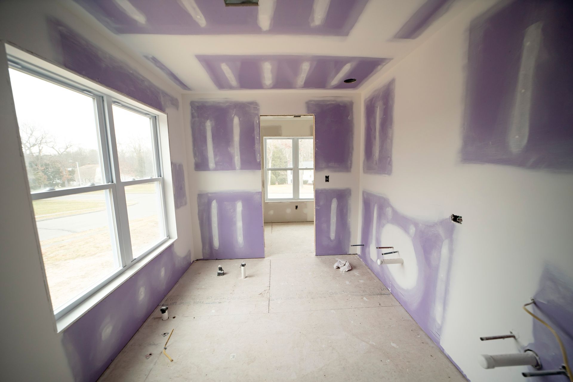 Room under construction, drywall installed; purple paper, unfinished walls and ceiling, window, open doorway.