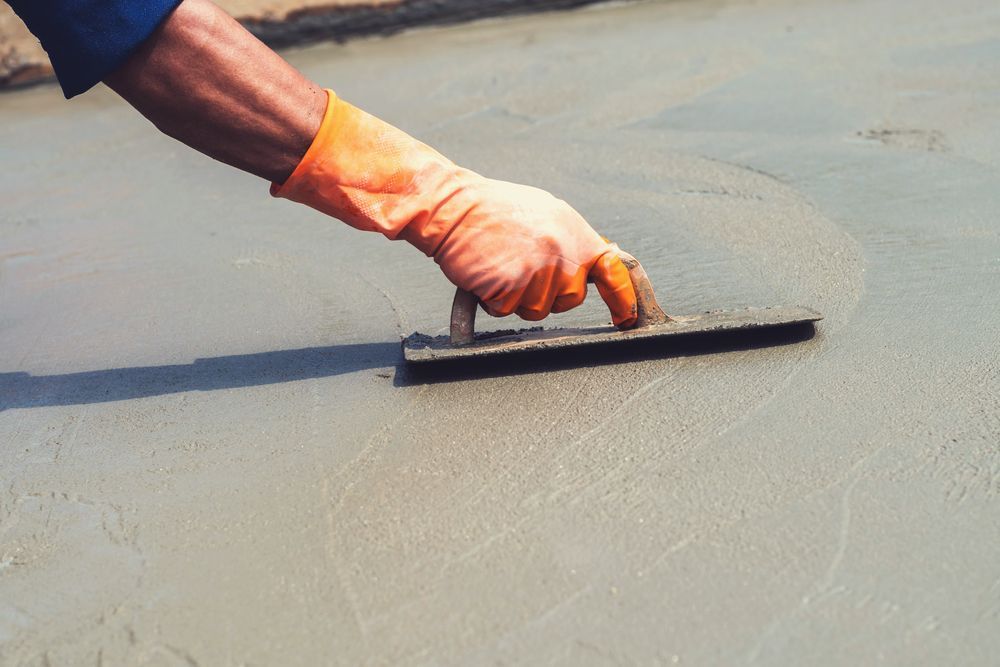 Hand in orange glove smoothing wet concrete with a trowel.