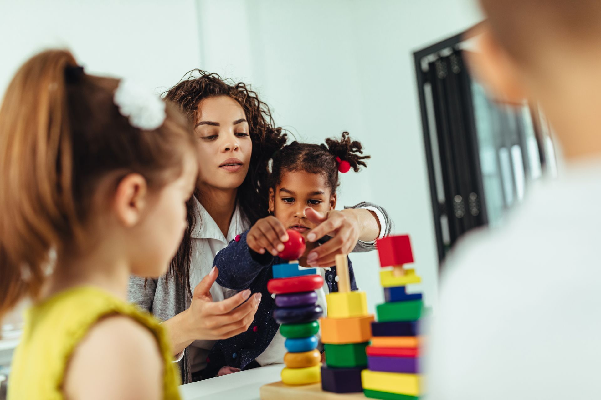 A woman is teaching a little girl how to stack wooden blocks.