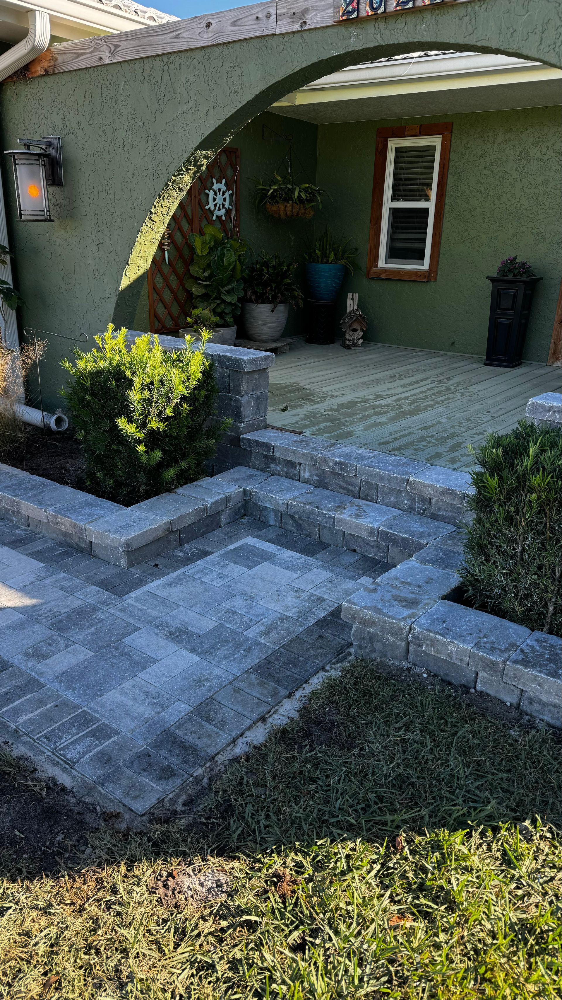 Stone steps leading up to a green stucco house with arched entryway and manicured landscaping.