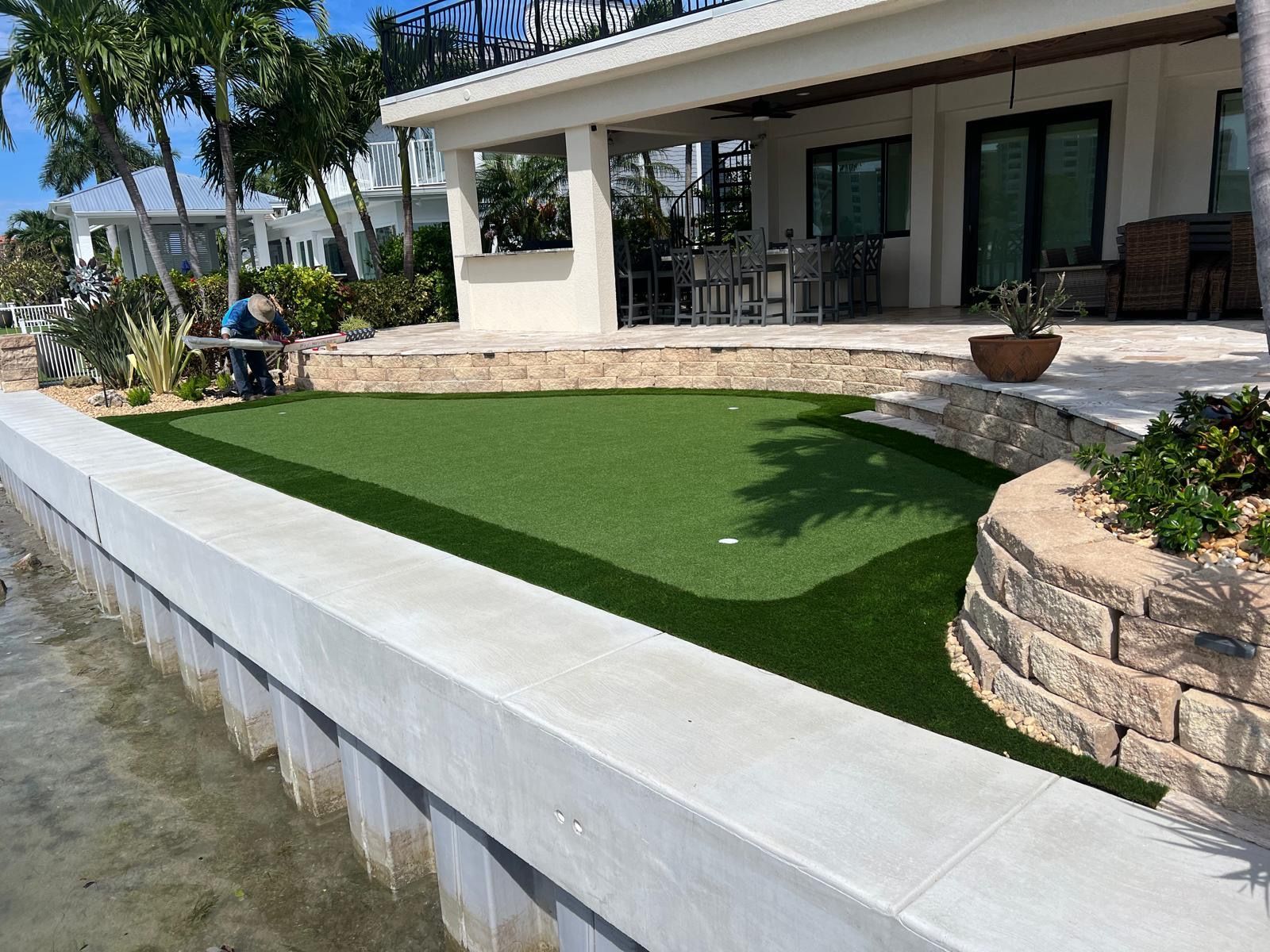 Artificial turf putting green next to a waterfront patio, with a concrete wall.