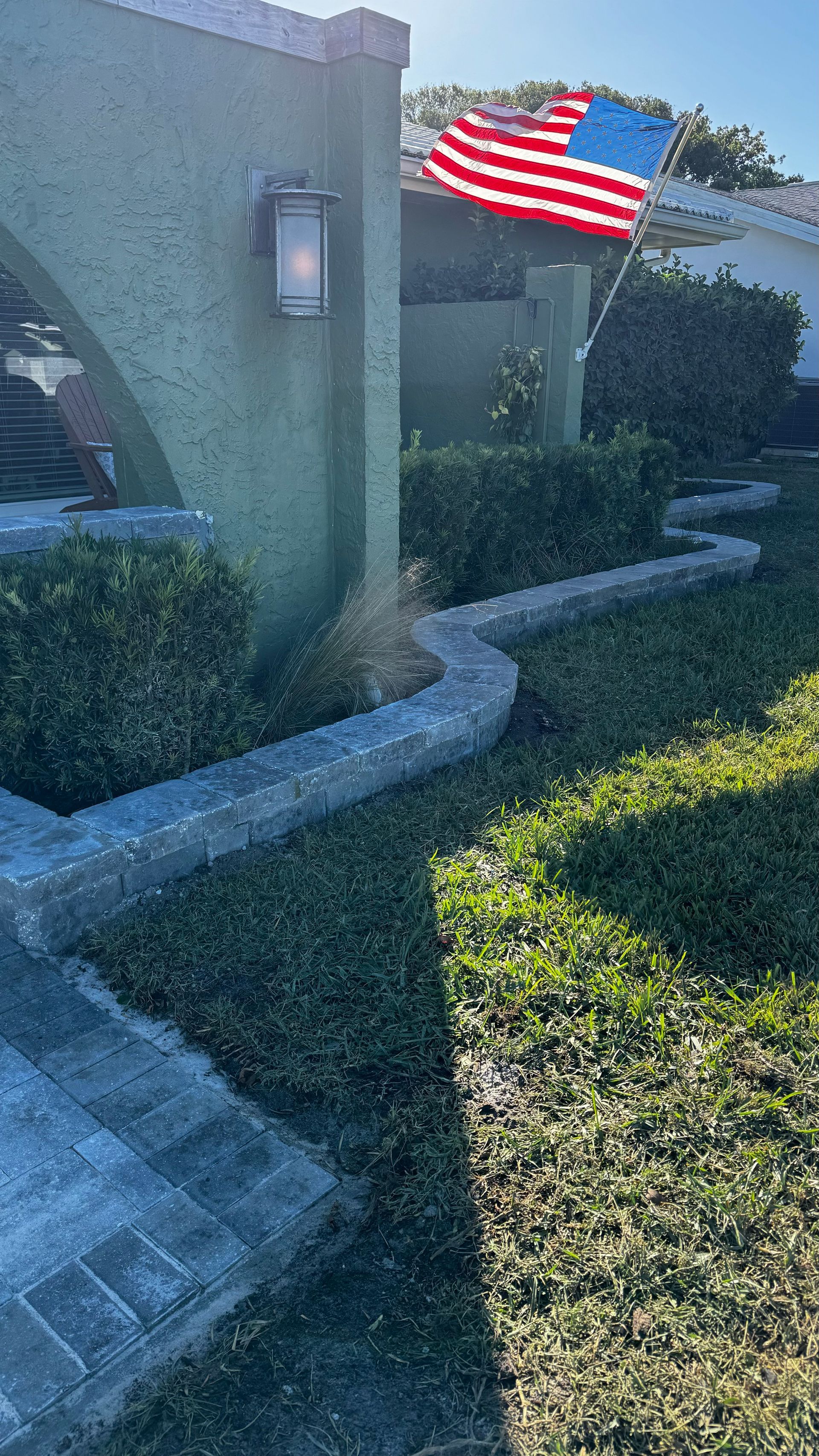Green house exterior with an American flag. Brick pathway, lawn, and bushes.
