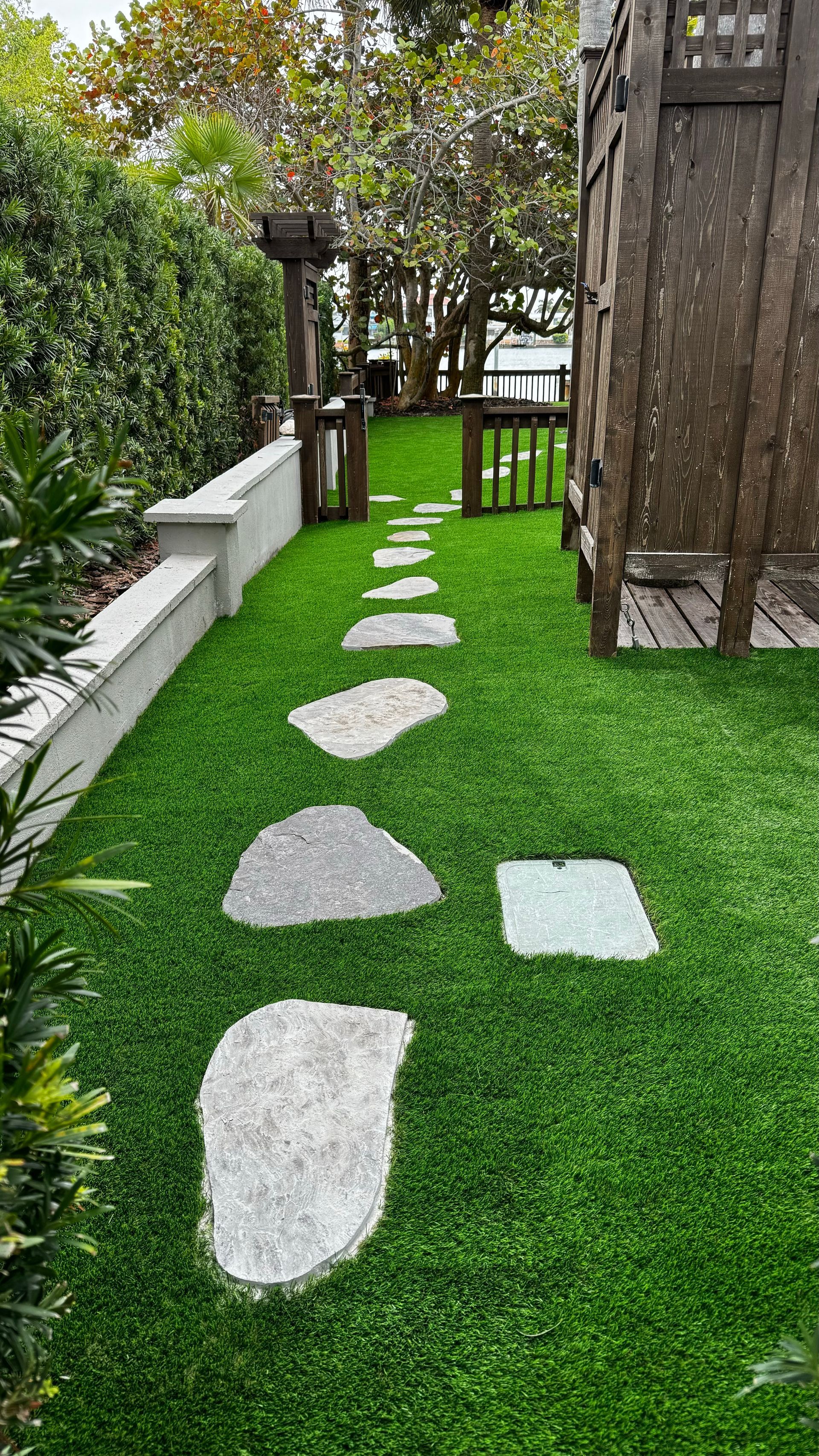 Stepping stones through green lawn lead to a wooden structure and gate in a garden setting.