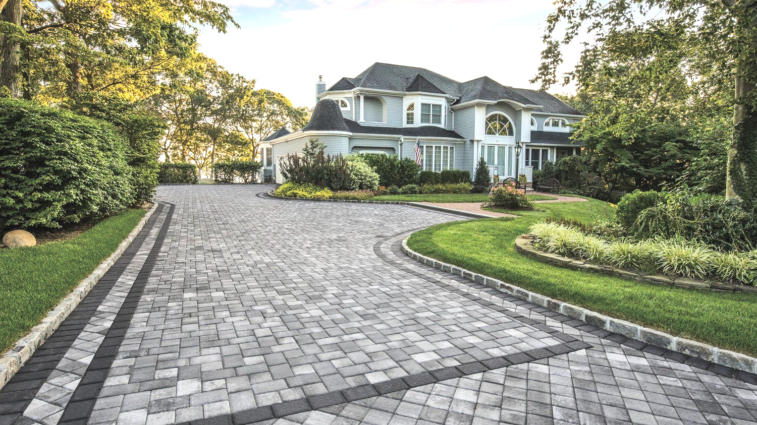 Elegant two-story house with a brick paver driveway, surrounded by landscaping and trees.