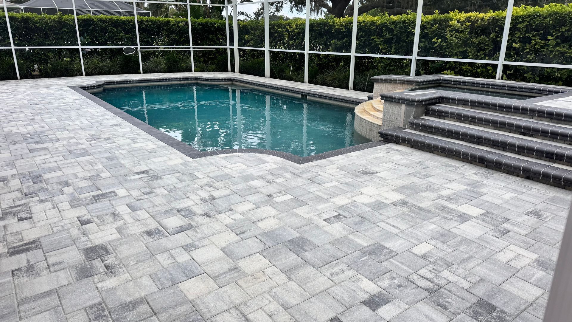 Pool with rectangular shape, surrounded by brick patio, steps, and screen enclosure.
