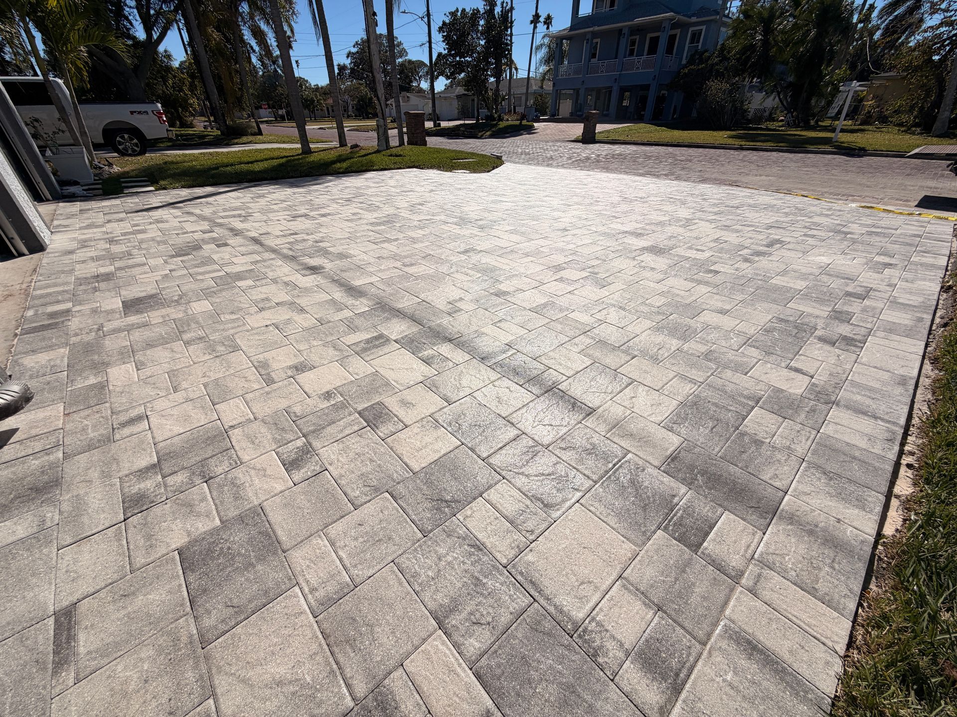 Stone paver driveway leading to a street, with a house in the background and a vehicle on the left.