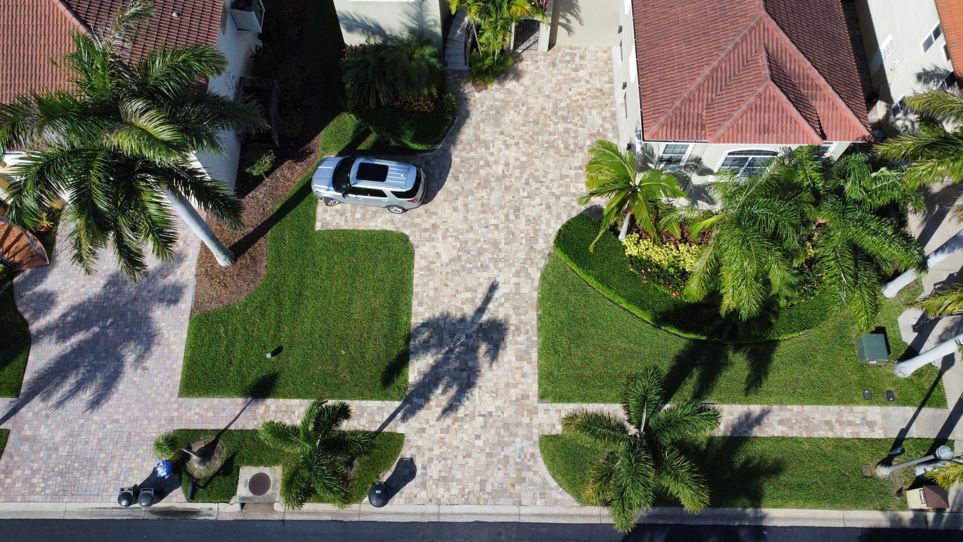 Aerial view of a driveway with a car, surrounded by green lawns and tropical landscaping.