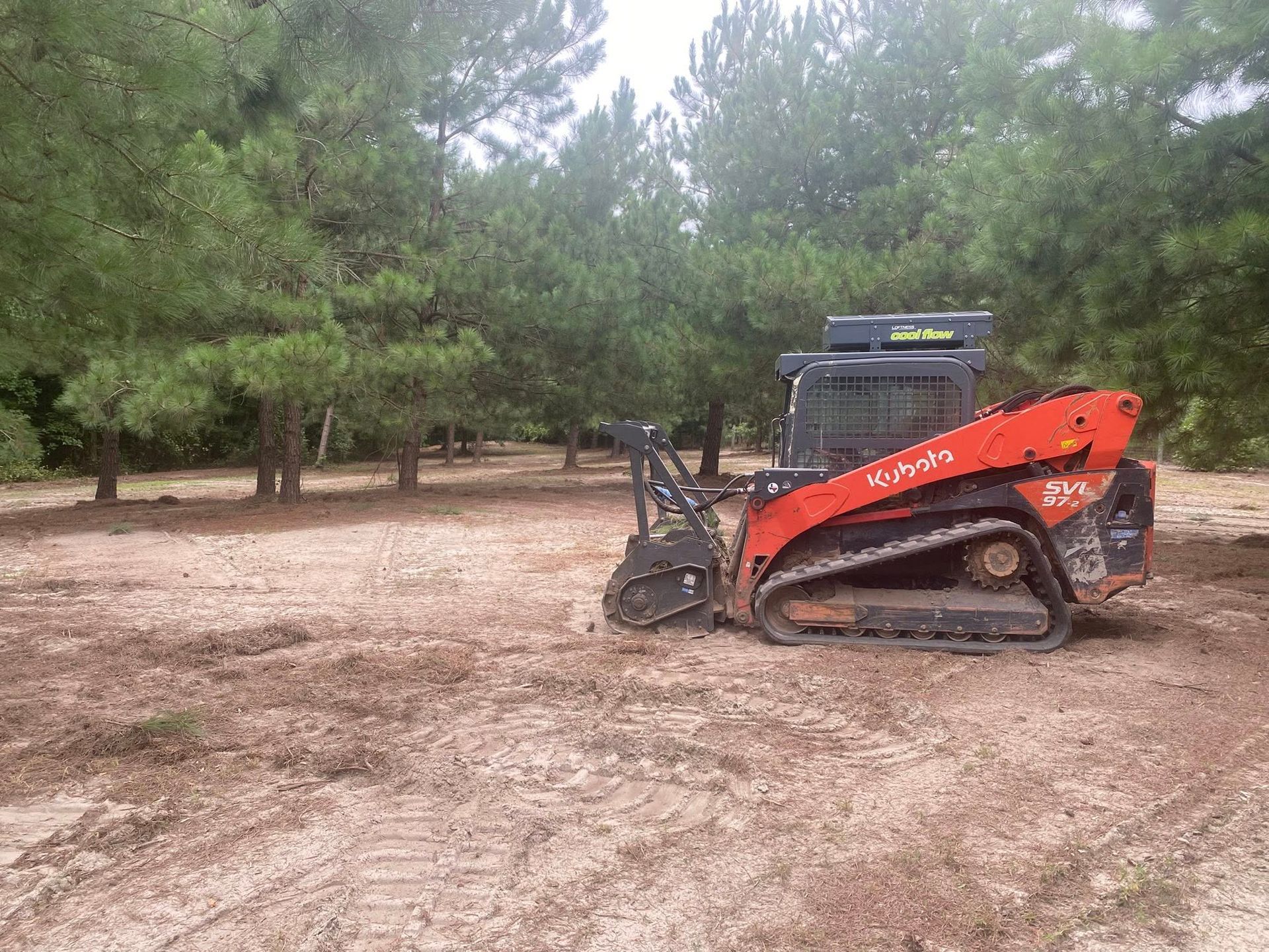 Orange Kubota track skid steer clearing land near trees.