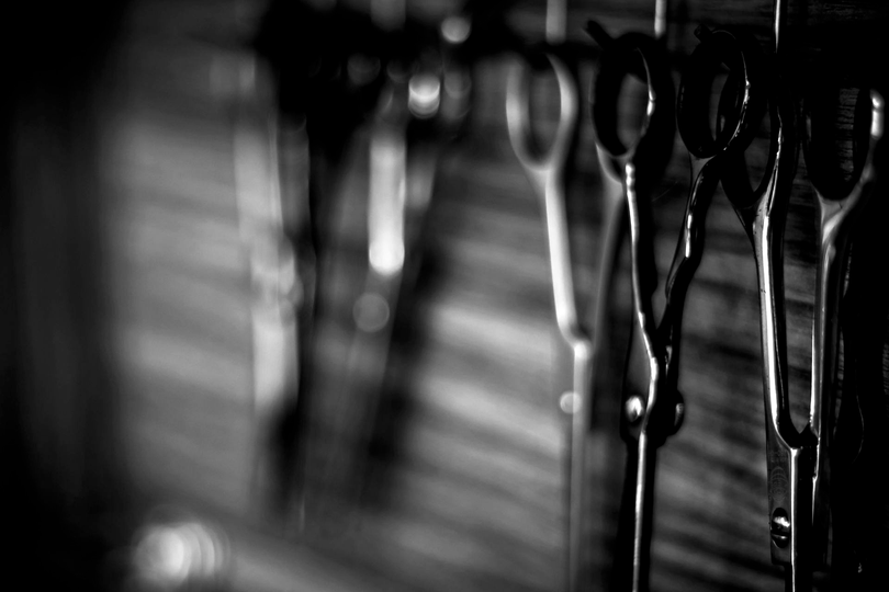 A close-up, black-and-white image of several pairs of professional hairdressing scissors hanging in a row.