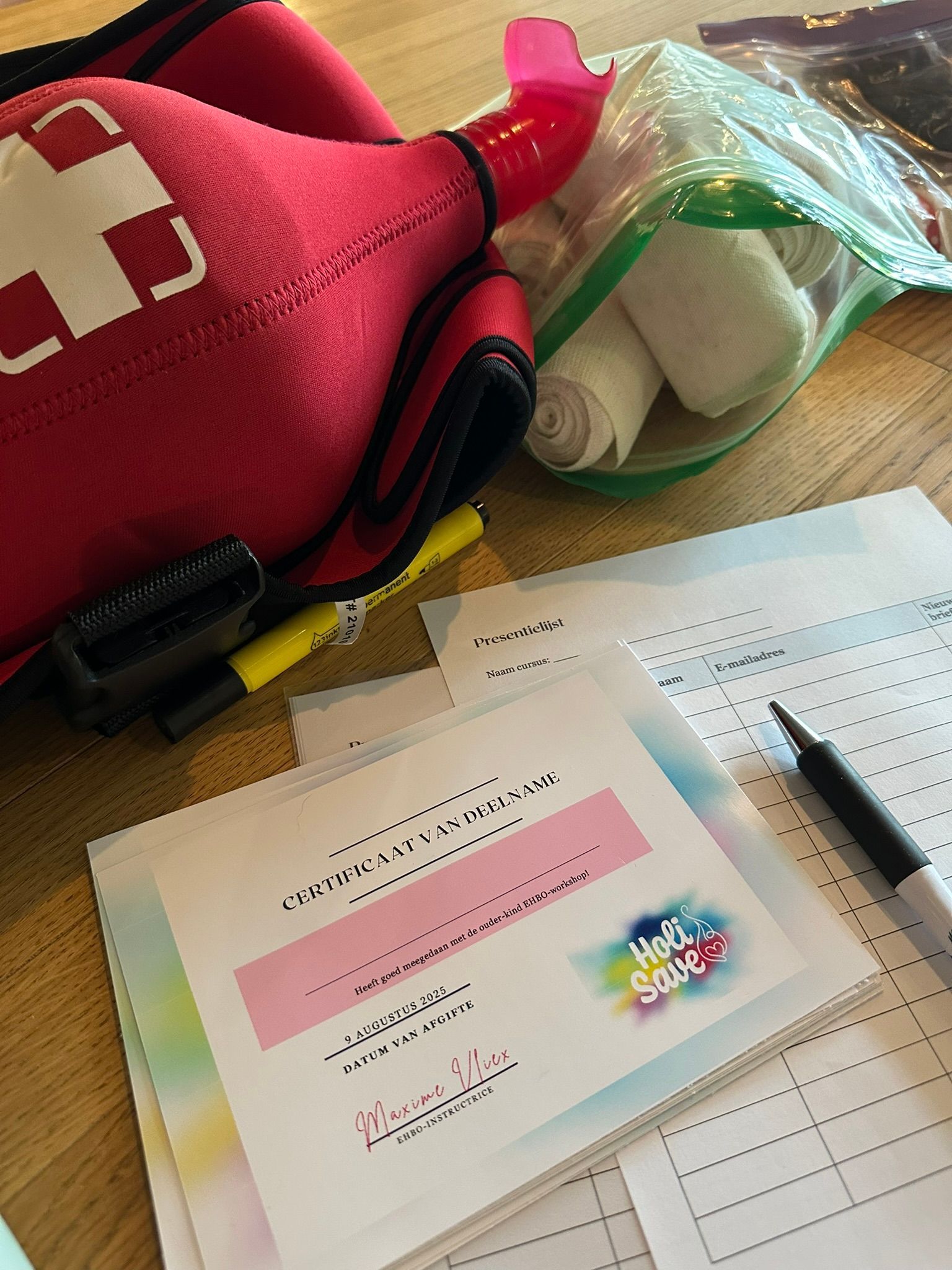 Rode EHBO-doos, verband, documenten en pen op een houten ondergrond.