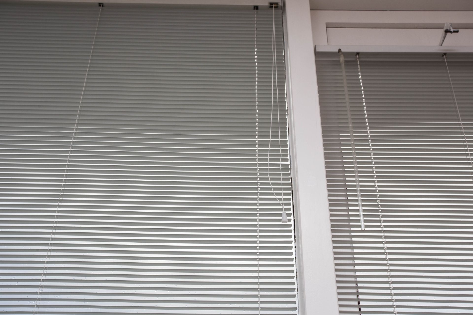 Silver blinds cover a window, partially obscuring light, viewed indoors.