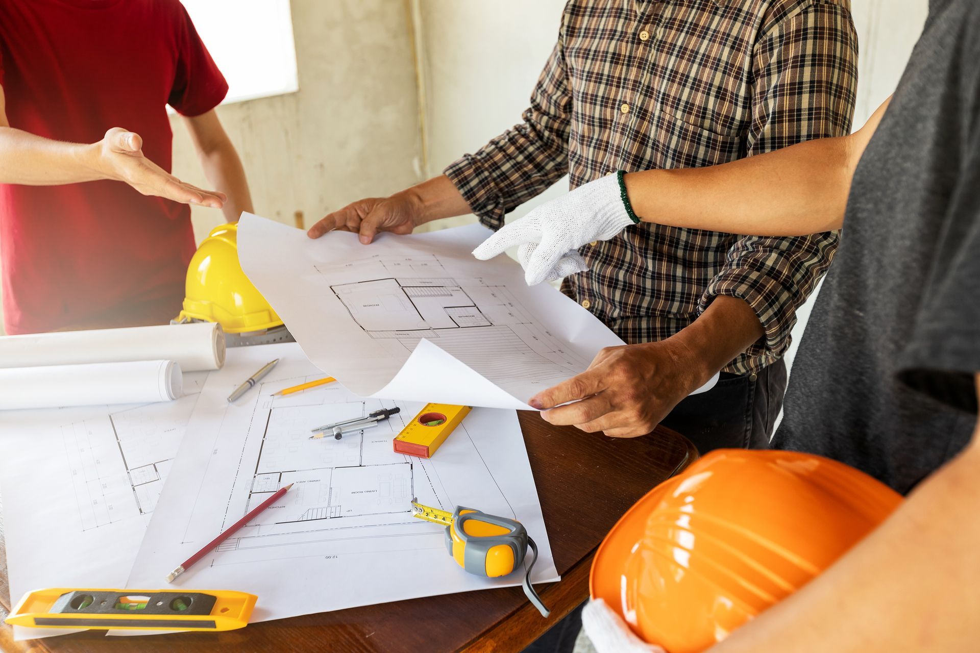 Construction workers examining blueprints at a table, with tools and hard hats, discussing plans.