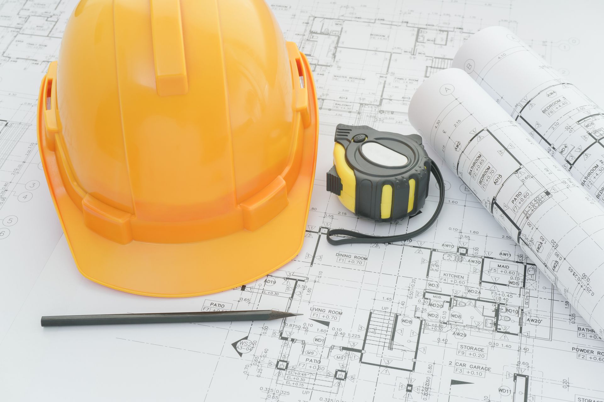 Yellow hard hat, rolled blueprints, tape measure, and pencil on architectural plans.
