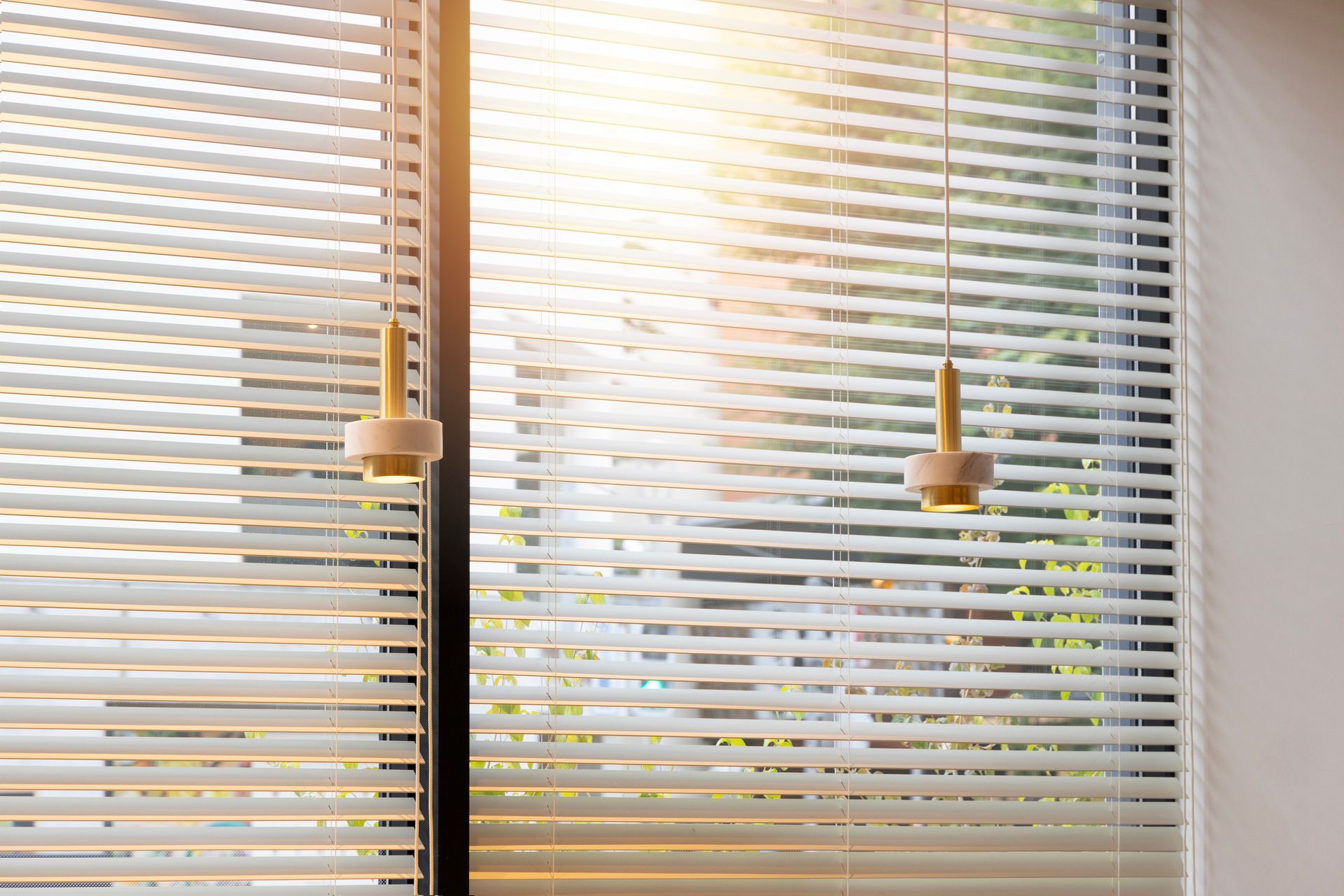 Sunlight streams through white horizontal blinds; two decorative pendant lights hang.