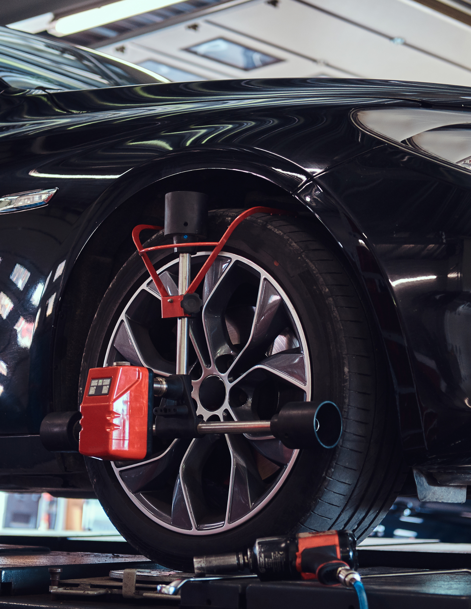 Car's front tire with wheel alignment equipment attached. Red, black, and silver machinery in a repair shop.