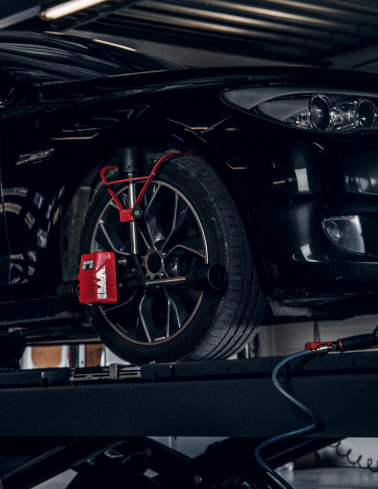 Black car on a lift, wheel alignment equipment attached to the tire in a garage.